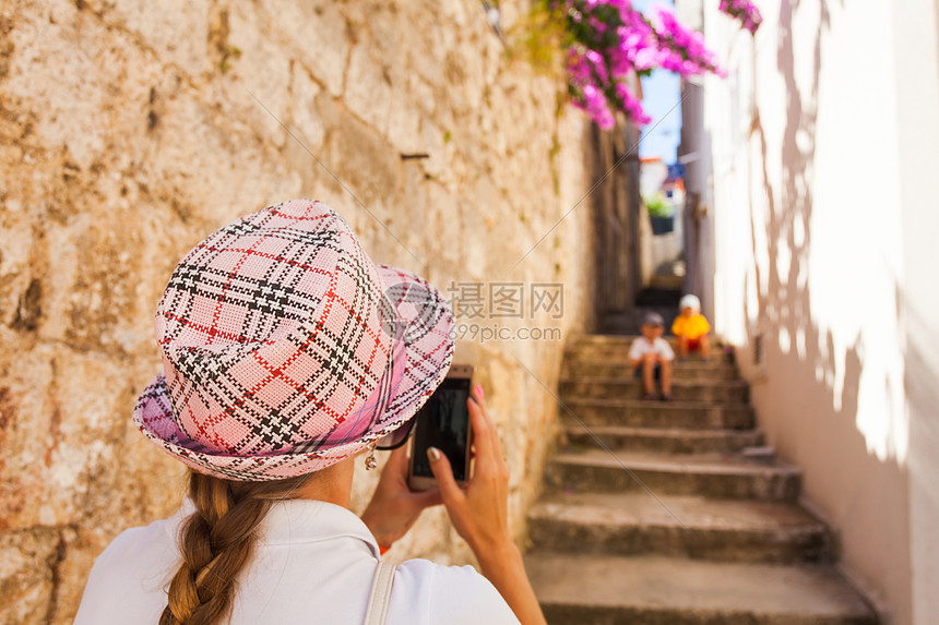 轻的女旅行者戴着顶支票帽子,条古老的狭窄街道上坐楼梯上的照片轻的女旅行者为她的孩子拍照图片