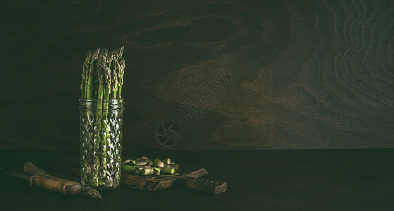 绿色芦笋装璃瓶里,水站桌子上,背景暗墙新鲜芦笋店春季季节蔬菜图片