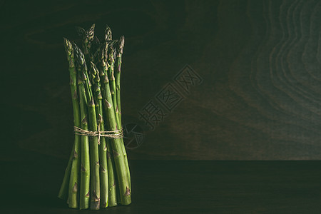绿色芦笋站黑暗的墙壁背景的桌子上春季季节蔬菜图片