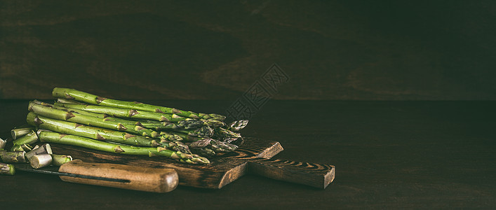 绿色芦笋木制切割板上,刀黑暗的乡村餐桌背景上图片