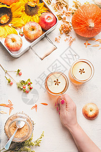 女手着璃杯,苹果热苹果酒苹果覆盖葡萄酒与苹果片白色桌与向日葵,南瓜秋叶,顶部视图秋天的季节享受图片