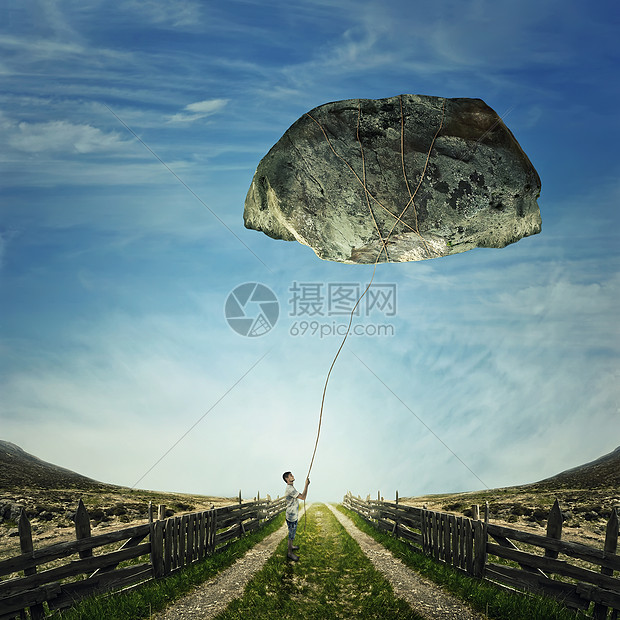 个轻的男孩站乡村道路上,着根绳子绑块巨大的石头上,个风筝生活压力