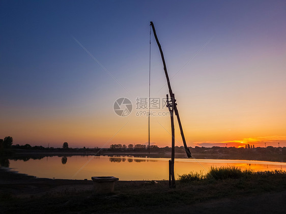 田园诗般的乡村景象与个古老的水井流行的称为鹳井老村庄的摩尔多瓦,也扫井沙多夫平静的日落天空反射湖上图片