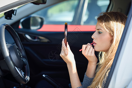 金发女人在车里对着镜子涂口红背景图片