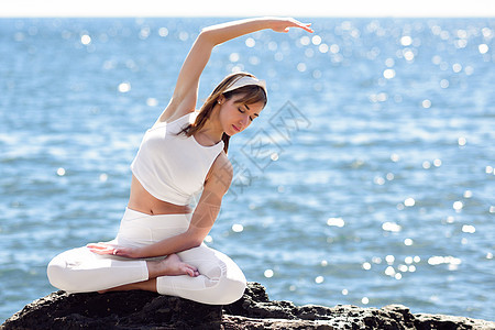 轻的女人海滩上瑜伽女穿着白色运动服,穿着莲花身材,的海洋背景图片