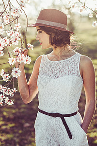 白色太阳帽春天花田里轻女人的肖像杏仁花开花了穿着白色连衣裙太阳帽的女孩背景