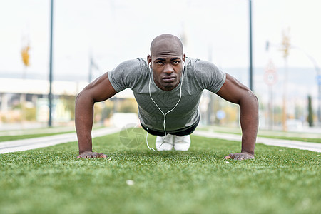 健身黑人锻炼俯卧撑,用耳机听音乐城市背景下的男模型交叉训练十多岁的非洲人街上户外锻炼图片