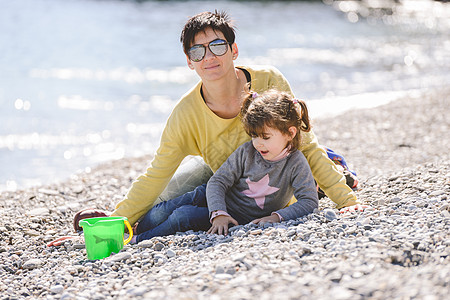 母亲她的小女儿海滩上玩得很开心的肖像高清图片