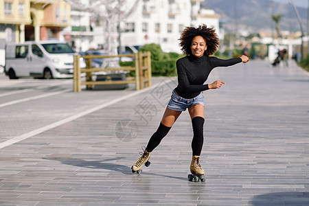 轻合身的黑人妇女溜冰鞋骑户外的城市街道上阳光明媚的日子里,微笑的女孩留着AFRO的发型图片
