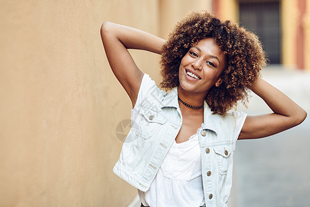 轻的黑人女人,阿夫罗的发型,街上的墙上微笑城市背景下穿休闲衣服的女孩图片