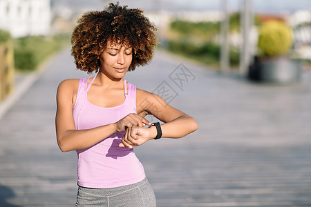 轻的黑人妇女积极的体育活动中用智能手表触摸触摸屏AFRO头发的女孩看着她的智能手表屏幕图片