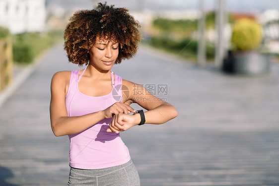 轻的黑人妇女积极的体育活动中用智能手表触摸触摸屏AFRO头发的女孩看着她的智能手表屏幕图片