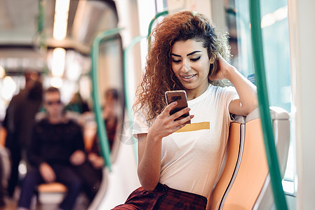 地铁里的阿拉伯女人看着她的智能手机穿着休闲衣服的阿拉伯女孩图片