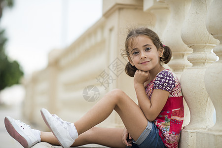 可爱的小女孩梳着辫子,坐户外的城市地板上图片