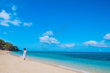 海滩上穿着白色连衣裙的女人穿着白色连衣裙的女人走蓝色的海边背景上图片