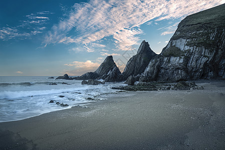 美丽的五颜六色的日落海滩景观与锯齿状的岩层背景图片