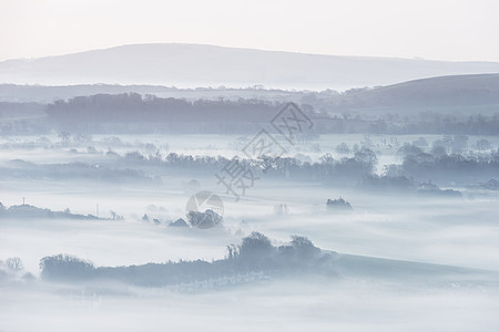 美丽的雾状英国乡村景观日出冬天,层层滚动田野背景图片