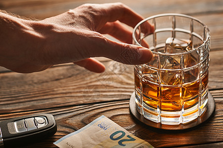 男人的手着杯威士忌酒精饮料,放着冰块汽车钥匙,放乡村木桌上喝酒开车酗酒的安全负责的驾驶理念图片