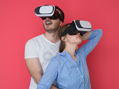 快乐的轻夫妇获得经验,用虚拟现实的VR耳机眼镜隔离红色背景图片