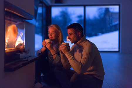轻的浪漫夫妇坐壁炉前的地板上,寒冷的冬天晚上家里喝茶聊天图片