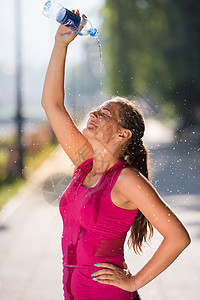 运动员女子跑步者阳光明媚的天城市慢跑后,瓶子里倒水她的头上背景图片