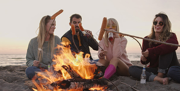 群轻的朋友深夜坐炉火旁,烤香肠,喝啤酒,聊天,玩得开心图片