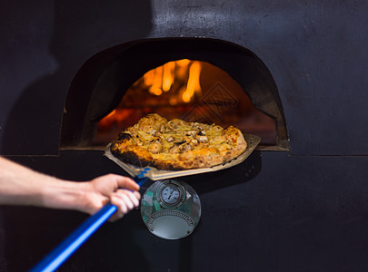 厨师用特殊的铲子把热披萨炉子里出来厨师炉子上热披萨图片