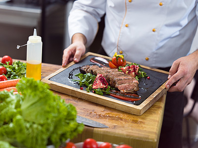 厨房厨师酒店餐厅厨房的厨师手特写,提供带蔬菜装饰的牛排特写厨师的手提供牛排背景