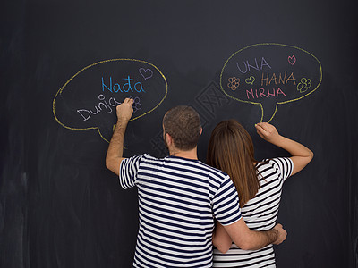 怀孕的夫妇黑板上写字轻的怀孕夫妇想着他们未出生的孩子的名字,并把它们写黑板上图片