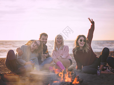 朋友们秋天的海滩玩得很开心快乐无忧无虑的轻朋友海滩上玩得开心,篝火旁喝啤酒,因为太阳开始彩色的过滤器图片