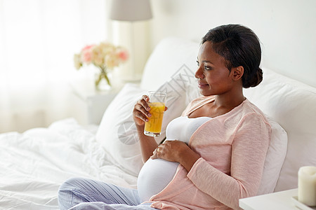 怀孕,人休息的快乐怀孕的非裔美国妇女家里床上喝橙汁孕妇床上喝橙汁图片