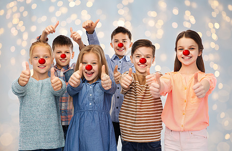 红鼻子日,慈善童的快乐的微笑儿童与小丑鼻子大拇指节日的灯光背景快乐的孩子们红鼻子日竖大拇指图片