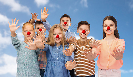 红鼻子日,慈善童的快乐的微笑孩子与小丑鼻子挥动手蓝天背景快乐的孩子们红鼻子的日子里挥手图片