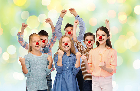 红鼻子日,慈善童的快乐的儿童朋友与小丑鼻子举拳头,庆祝胜利的绿灯背景红鼻子日快乐的孩子图片