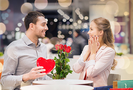爱情,浪漫,情人节,夫妇人的快乐的轻人带着红花送礼物给微笑的女人购物中心的咖啡馆快乐的情侣商场里礼物鲜花图片