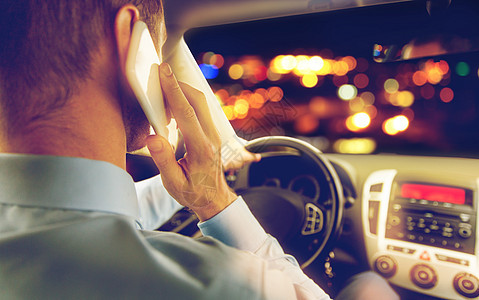 交通,商务旅行,技术人的男子驾驶汽车打电话智能手机夜间城市灯光背景男子驾驶汽车呼叫智能手机图片