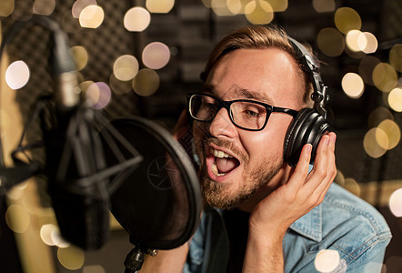 音乐,表演业务,人声音男歌手戴着耳机麦克风节日灯光下的录音棚唱歌带耳机的男人录音棚唱歌背景图片