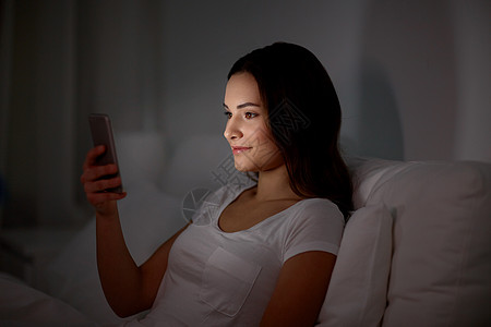 技术,互联网,沟通人的快乐的微笑轻妇女与智能手机家里的晚上快乐的轻女人,晚上床上智能手机图片