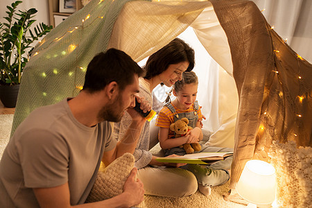 家庭,潮格人的快乐的母亲,父亲小女儿阅读书与火炬灯孩子们的帐篷晚上家孩子们家帐篷里快乐的家庭读物图片