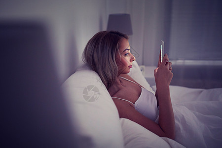 技术,互联网,沟通人的轻的女人智能手机上发短信家里的卧室晚上轻的女人家里卧室的床上智能手机图片