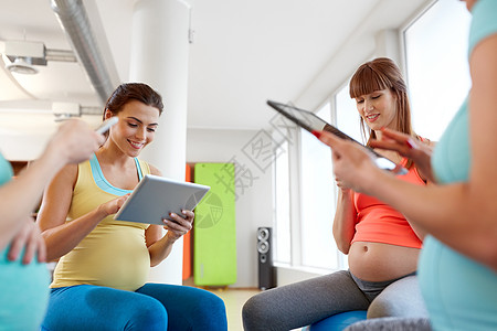 怀孕,健身技术群快乐的孕妇,平板电脑智能手机坐健身房的运动球上快乐的孕妇健身房用平板电脑图片