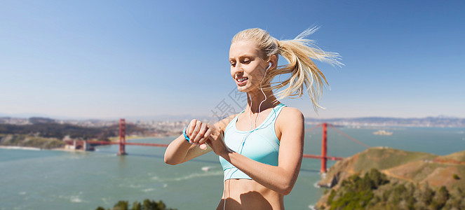 运动,技术健康的生活方式微笑的轻妇女与健身跟踪器耳机锻炼金门大桥旧金山海湾背景金门大桥上健身追踪器的女人背景图片
