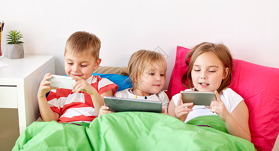 智能家童,技术家庭孩子们家里的床上平板电脑智能手机家里平板电脑智能手机的孩子躺床上家里平板电脑智能手背景
