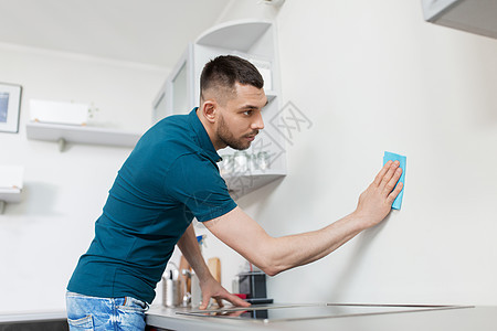 家庭人的男人家里厨房用布清洁墙壁家里厨房里抹布清洁墙的男人家里厨房里抹布清洁墙的男人图片