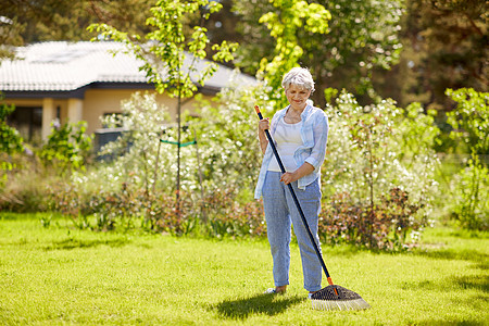 园艺人的快乐的老年女子与草坪耙工作夏季花园草坪耙的老年女子花园工作草坪耙的老年女子花园工作图片