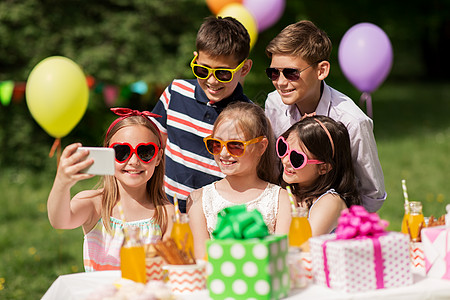 假期,童技术快乐的孩子戴着太阳镜,夏季花园的生日聚会上用智能手机自拍快乐的孩子生日聚会上自拍图片