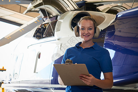 女航空工程师的肖像与剪贴板进行检查直升机机库图片