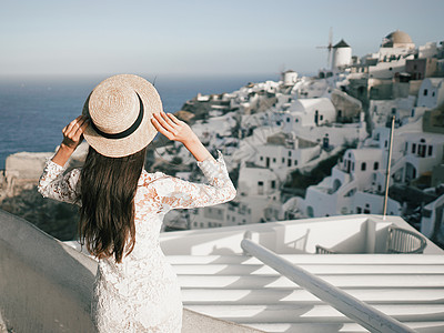 穿着白色连衣裙草帽的快乐女人桑托里尼岛享受假期OIA看爱琴海欧洲夏季旅游目的地希腊岛屿图片