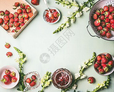 框架与新鲜草莓科兰德碗与果酱罐勺子厨房桌子背景与花园花卉,顶部视图夏季浆果保存季节当地机食品图片