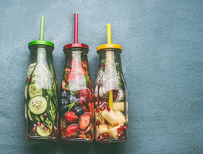 各种彩色注入水的瓶子与水果浆果,黄瓜,草药饮料吸管灰色背景,顶部视图美味的夏季清洁饮料,健康的生活方式健身图片